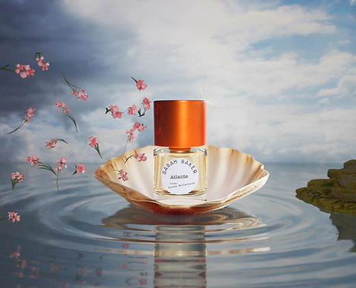 The Art + Olfaction Awards finalist, Atlante by Sarah Baker, with an orange cap sits inside an open seashell on water, surrounded by pink flowers against a cloudy sky backdrop. Its salty fragrance perfectly complements the serene setting.