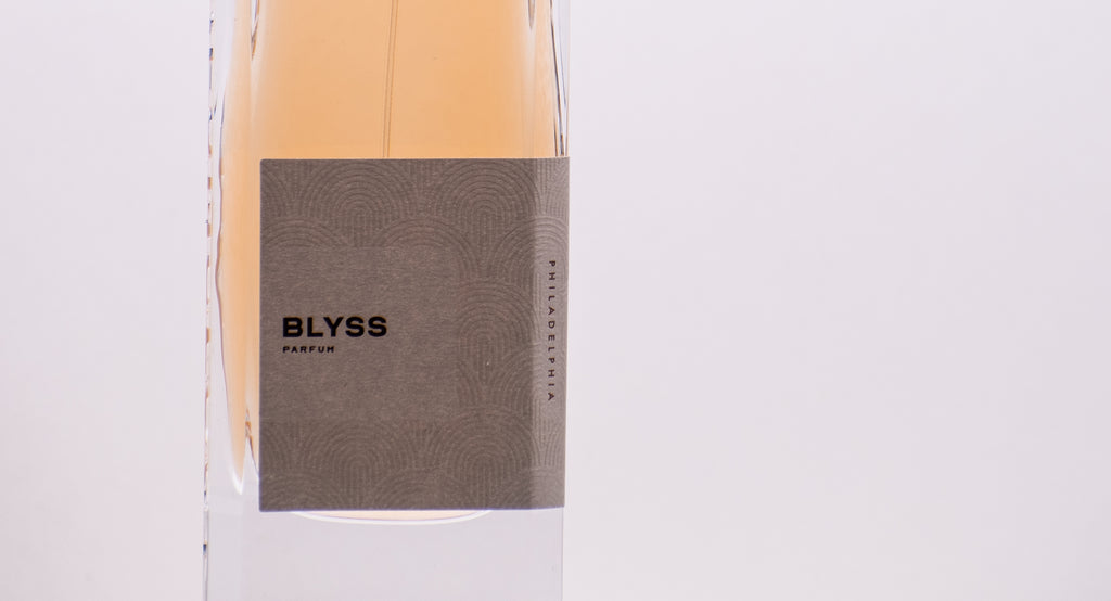 Close-up of a perfume bottle with a label reading "BLYSS PERFUMOLOGY" against a light background, showcasing the essence of Blyss fragrance crafted with high-quality ingredients.