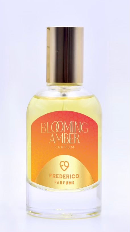 A bottle of Frederico Parfums’ Blooming Amber with a gold cap and an orange-yellow gradient label, known for its long-lasting scent.