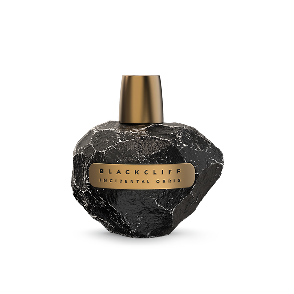 A black stone-textured perfume bottle with a gold cap and label, reading "Incidental Orris" by Blackcliff, captures the essence of forest bathing in its fragrance.