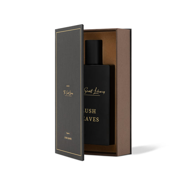 A black perfume bottle labeled "Lush Leaves" rests in an elegant, partially open black and gold box, exuding a hint of cardamom for a subtly exotic touch from The Scent Library.