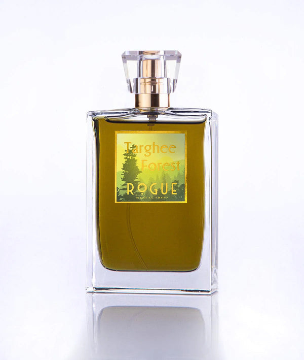 A clear glass perfume bottle with a gold and green label reading "Targhee Forest, Rogue Perfumery." The perfume inside is a greenish liquid, evoking woody notes of pine and cedar. The bottle has a geometric, transparent cap.