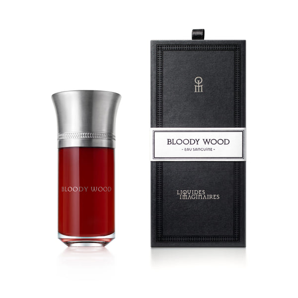 A bottle of Bloody Wood perfume with a dark red liquid inside sits next to its tall, rectangular black packaging with a white label, a creation by the renowned perfumer Shyamala Maisondieu for Liquides Imaginaires.