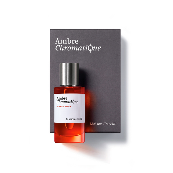 An amber-colored bottle labeled "Ambre Chromatique," a luxurious vegan perfume by Maison Crivelli, is placed on a matching box adorned with the same text.