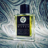 A clear glass bottle of Gallagher Fragrances' "Amongst Waves" perfume stands on a marbled surface. The black label lists ingredients like green apple, honeydew, lime zest, sea salt, patchouli, and aquatic notes.