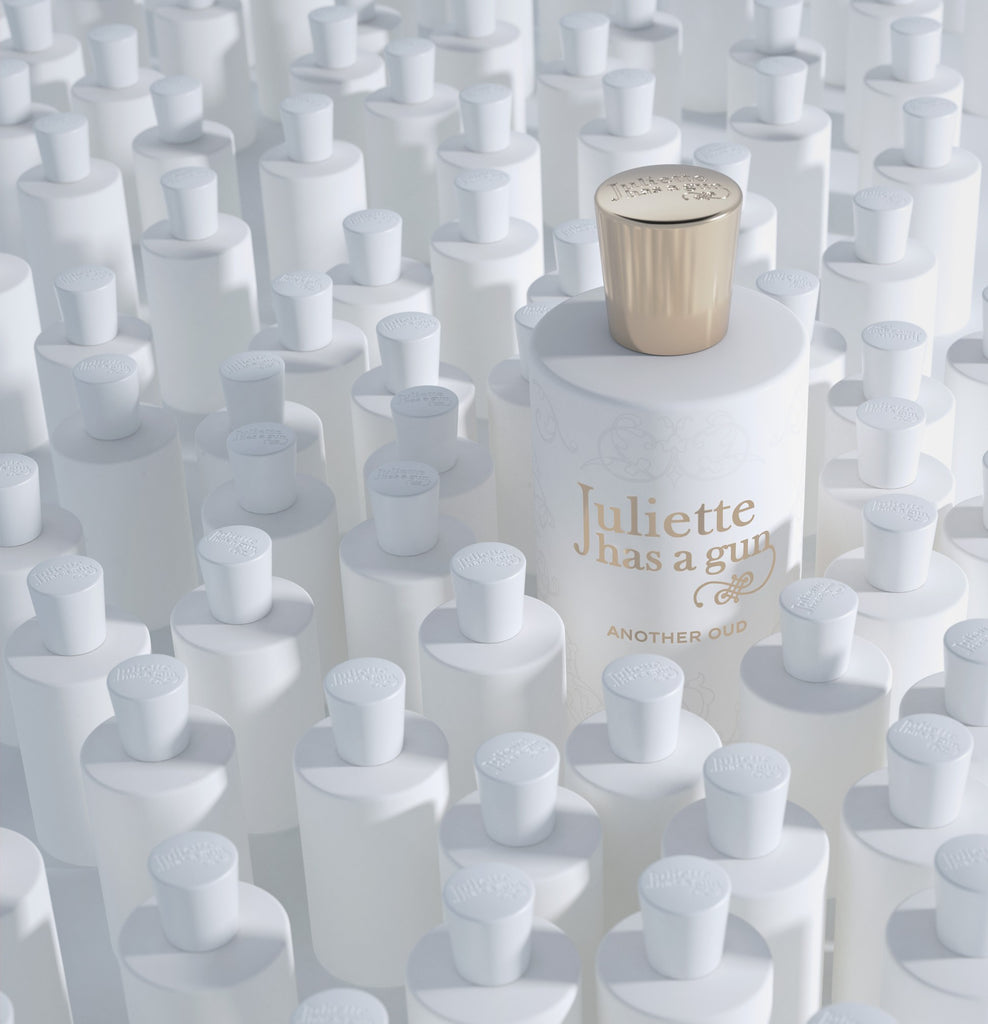 A single white bottle of "Another Oud" by Juliette Has A Gun with a gold cap stands out among numerous white bottles with white caps, each sharing the same design and shape, yet distinguished by its luxurious touch of oud wood.