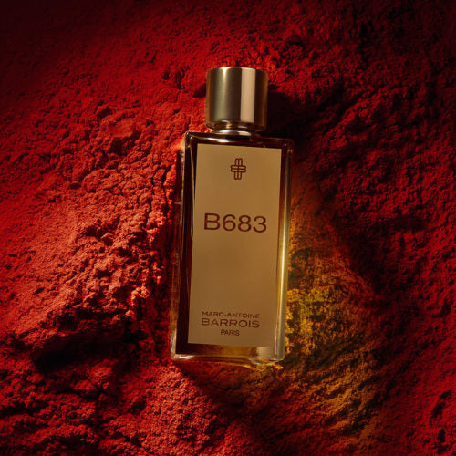 A bottle of B683 by Marc-Antoine Barrois positioned against a textured, red background, evoking the essence of leather and sophisticated fragrance.