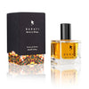 A 30 ml bottle of Baruti Berlin im Winter extrait de parfum stands next to its black box with colorful bottom accents. The intoxicating fragrance, featuring an amber-colored liquid and a black cap, brings a modern edge to your scent collection.