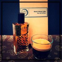 A bottle of Black Velvet Cafe perfume by 4160Tuesdays and a glass cup of espresso are placed on a decorative brown surface in front of a box labeled "Black Velvet Cafe Eau de Parfum by 4160Tuesdays.