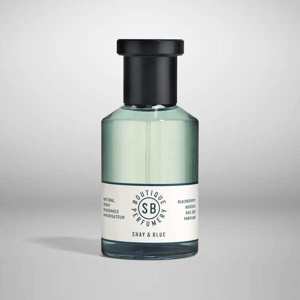A bottle of Shay and Blue Blackberry Woods with a black cap and a white label displaying the brand name and product information. Partially filled with greenish-blue liquid, this vegan fragrance is also responsibly sourced, ensuring both elegance and ethical integrity.