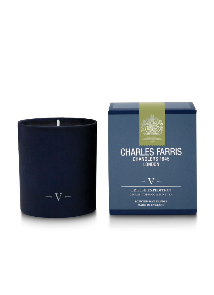A black candle with a 'V' symbol in front of a blue box labeled, "Charles Farris Chandlers 1845 London," features the Charles Farris British Expedition scented candle with notes of Clove, Tobacco & Mint Tea.