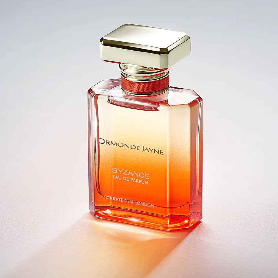 A bottle of Ormonde Jayne Byzance Eau de Parfum features a rectangular glass design, a gold-colored cap, and gradient orange-to-clear liquid inside. The text on the bottle reads "Created in London." The scent reveals an amberesque warmth that blends seamlessly with a subtle gourmand touch.