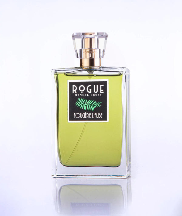 A clear glass bottle of Rogue Perfumery's "Fougere L'Aube" fragrance reveals a green citrus-infused, greenish-yellow liquid inside, topped with a gold-colored cap and a transparent cover.