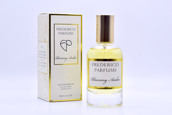 A 50 ml bottle of Frederico Parfums' "Blooming Amber" Eau De Parfum, known for its long-lasting, solar fragrance, stands beside its matching box packaging.