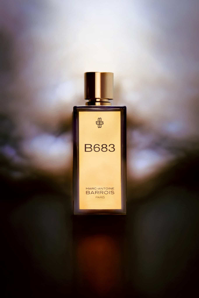 A bottle of Marc-Antoine Barrois B683 Extrait with a golden cap, exuding a woody-leathery accord, set against a blurred background.