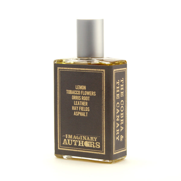 A glass bottle of perfume named "The Cobra & The Canary" by Imaginary Authors, capturing the decadence and desolation of Palm Springs race tracks with notes of lemon, tobacco flowers, orris root, leather, hay fields, and asphalt that evoke the spirit of the 1964 Shelby Cobra Roadster.