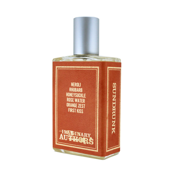 A Sundrunk perfume bottle by Imaginary Authors, rectangular in shape, adorned with a silver cap and an orange label listing scents such as rhubarb, neroli, honeysuckle, rose water, orange zest, and the essence of first kiss.
