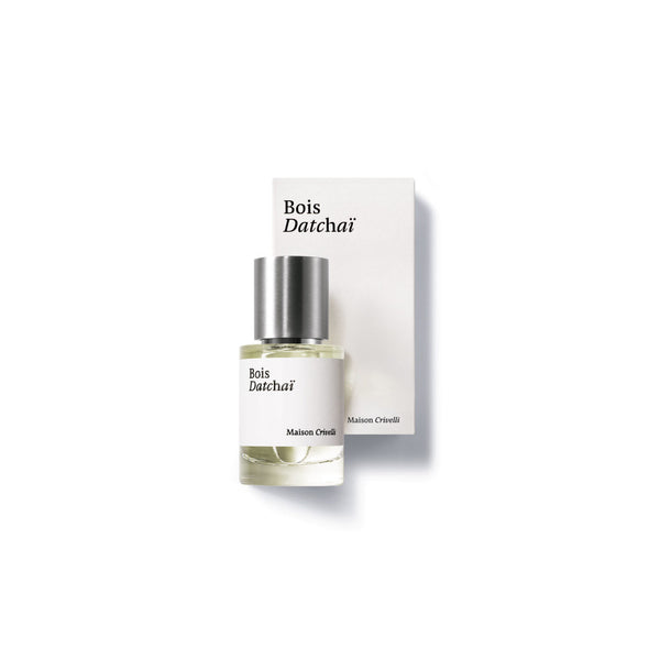 A small perfume bottle labeled "Bois Datchai" by Maison Crivelli is placed in front of its matching white box. The bottle has a silver cap and contains a light-colored woody fruity eau de parfum, infused with notes of black tea absolute.