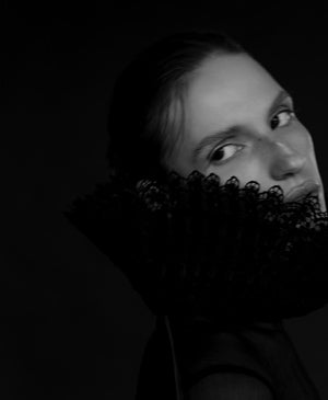 Black and white portrait of a person with a lace ruff around their neck, gazing sideways, exuding an air of mystery reminiscent of Beaute Du Diable by Liquides Imaginaires. The dark background intensifies the aura.