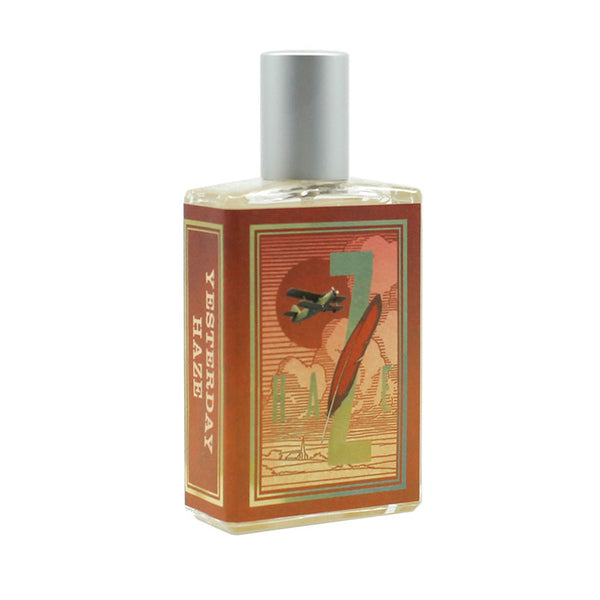 A bottle of Imaginary Authors' Yesterday Haze fragrance with a squared shape, metallic cap, and detailed label featuring artistic graphics in warm tones. This seductive scent, inspired by Lenora Blumberg's creative vision, captures the essence of nostalgia with every spritz.