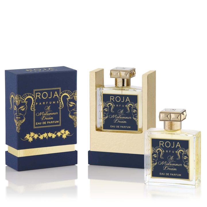 A perfume set featuring "Roja Parfums A Midsummer Dream EDP." One bottle is displayed inside the open box, while another is outside. The packaging, adorned in navy blue and gold with ornate designs, hints at the delicate notes of grapefruit and rose that lie within.