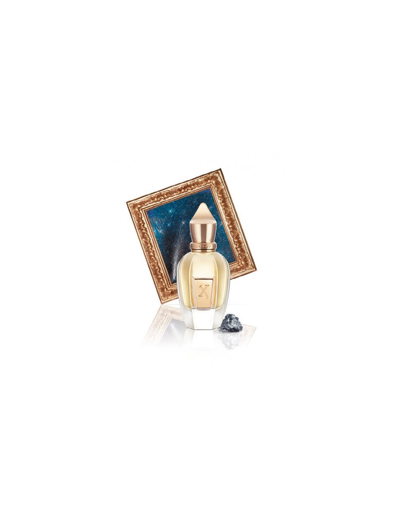 A bottle of Xerjoff Uden stands in front of a tilted decorative frame, with a small gemstone placed to its right.
