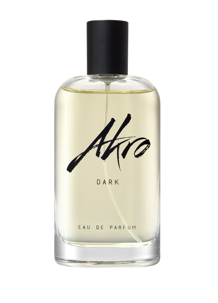 A clear glass perfume bottle with a black cap, labeled "Akro DARK," containing a light yellow liquid that exudes a mature sensuality and an addictive chocolate fragrance.