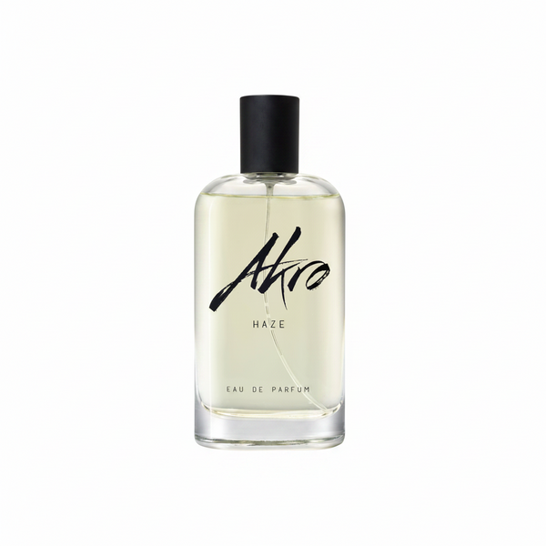 A clear glass bottle of HAZE Eau de Parfum by Akro, featuring a black cap and black text, exuding a refined smoky scent perfectly complemented by the herbal aroma of Clary sage.