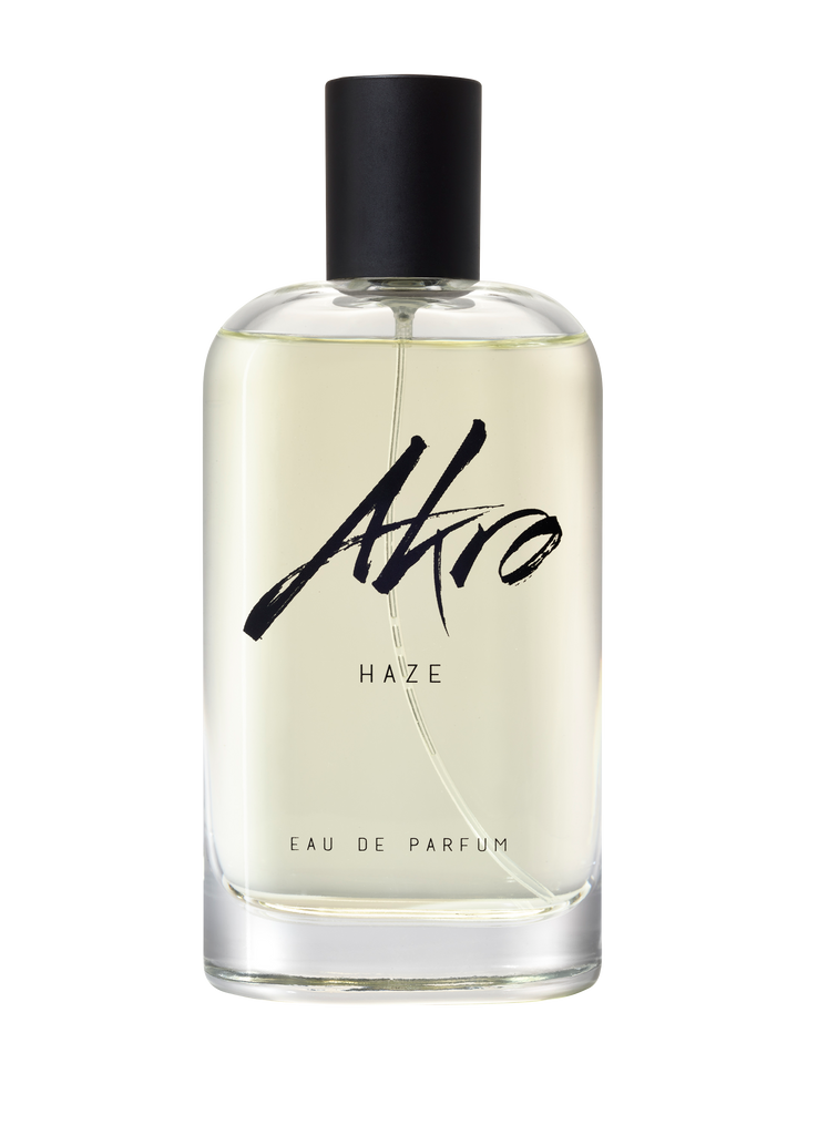 A clear glass bottle of HAZE Eau de Parfum by Akro, featuring a black cap and black text, exuding a refined smoky scent perfectly complemented by the herbal aroma of Clary sage.