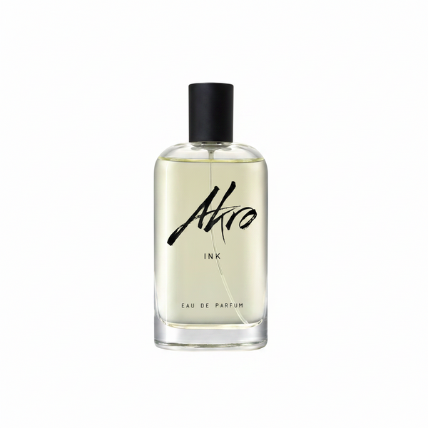 A clear glass bottle of INK by Akro, a unique tattoo fragrance with a black cap and black text on the label. The light yellow liquid inside captures the essence of body decoration.