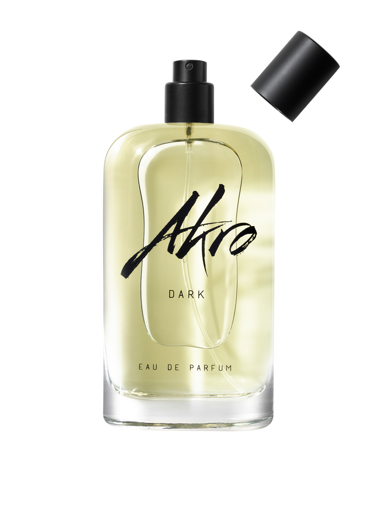 A clear glass bottle of Akro DARK Eau de Parfum with a black spray top and detachable cap, exuding mature sensuality with its addictive chocolate fragrance.