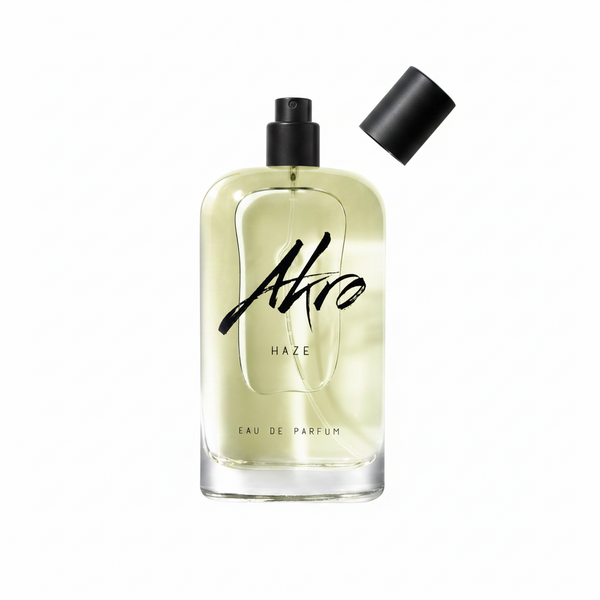 A clear glass bottle of Akro HAZE Eau de Parfum, adorned with black text on the front, showcases a light yellow liquid inside. Topped with a black cap, this addictive chill fragrance exudes a fresh smoky scent that intrigues and captivates.