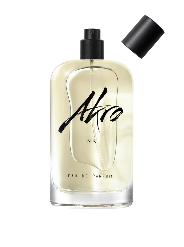 A clear glass bottle of INK by Akro Eau de Parfum featuring a black spray nozzle, with its detached black cap placed to the side, capturing the essence of its unique tattoo fragrance.