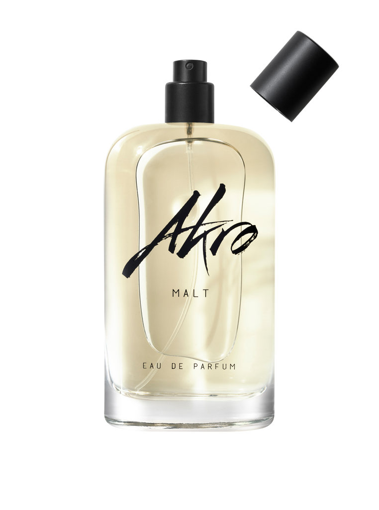 A clear glass bottle of MALT Eau de Parfum by Akro, exuding a rich whisky fragrance with a hint of smoky aroma, stands with its black spray cap removed and placed nearby.