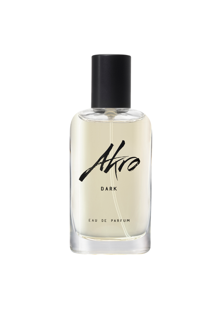 A transparent bottle of Akro DARK eau de parfum with a black cap and black text on the front, exuding a dark chocolate fragrance that captures mature sensuality.