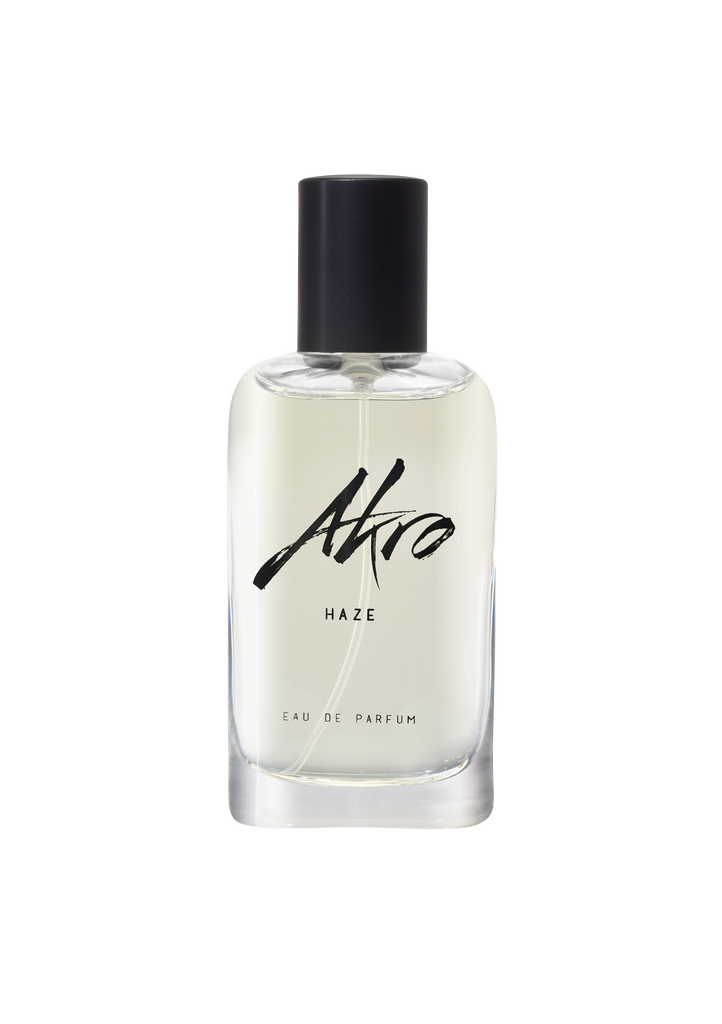 A clear glass perfume bottle, featuring a black cap and labeled with "Akro" and "HAZE," exudes a smoky scent with hints of clary sage.