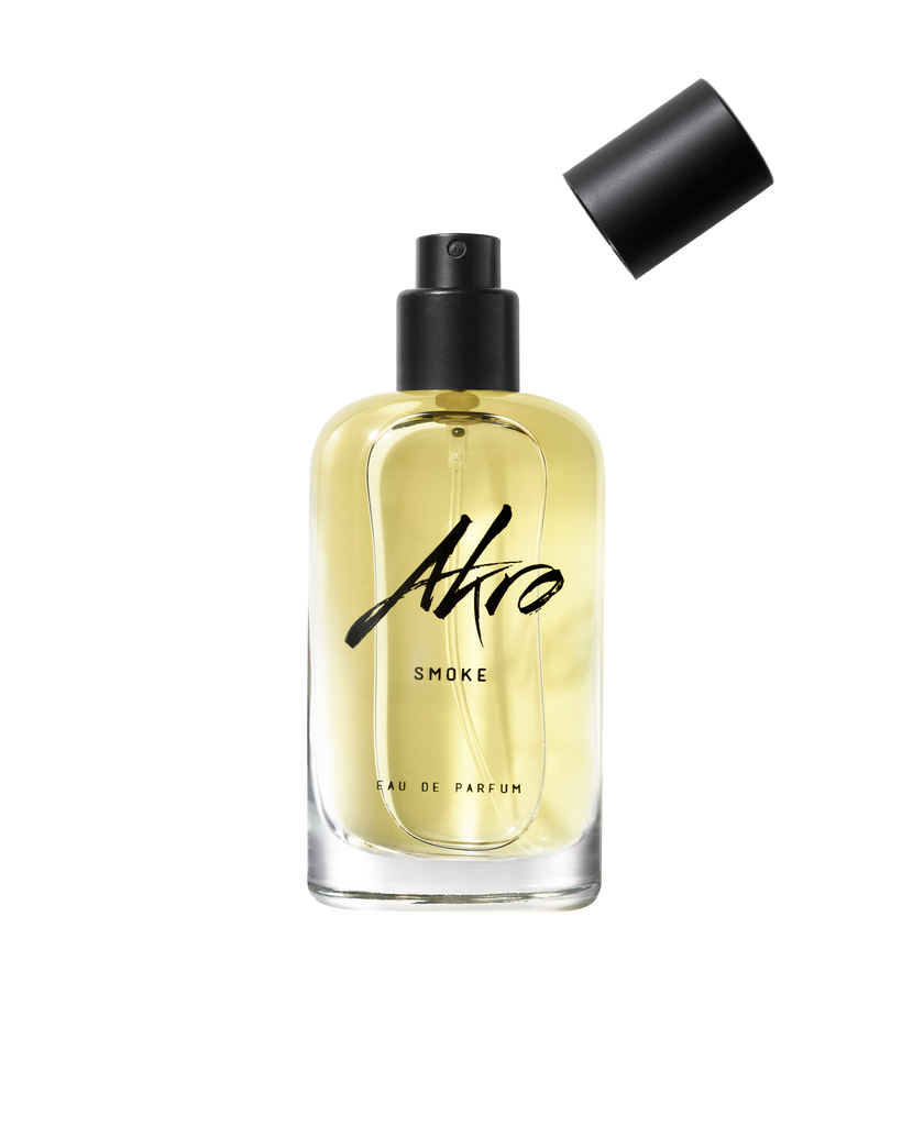 A bottle of SMOKE Eau de Parfum by Akro, featuring a black spray nozzle and a detachable black cap. This unisex perfume, belonging to the aromatic family, contains a light yellow liquid that exudes a rich tobacco fragrance.