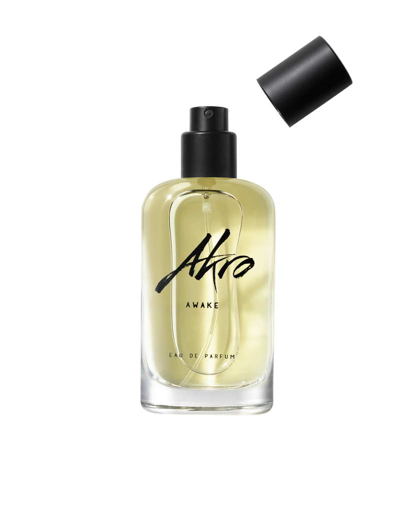 A clear bottle of Akro AWAKE unisex Eau de Parfum with a black spray nozzle and the cap removed, displaying light yellow liquid inside, emanates an energizing coffee fragrance.