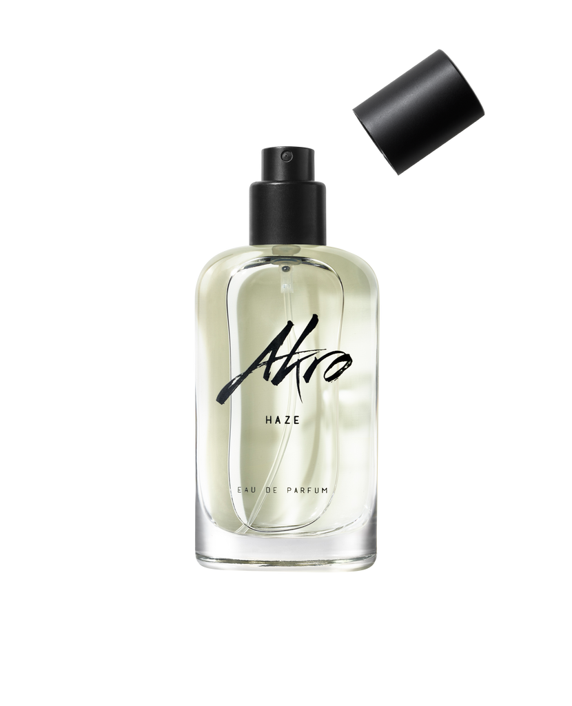 Clear glass bottle of Akro HAZE Eau de Parfum with a black cap removed and positioned above the bottle, exuding a smoky scent.