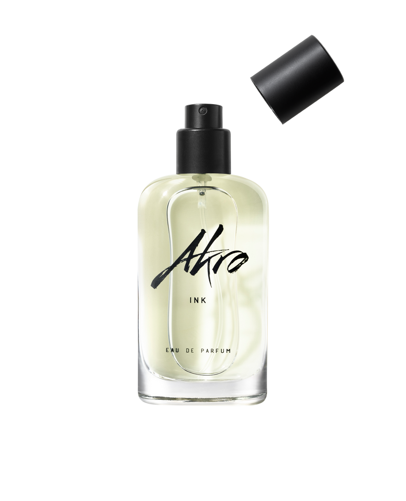 A clear bottle of Akro INK Eau de Parfum, adorned with black text on the front and featuring a detached black cap above it, captures the essence of a tattoo fragrance.