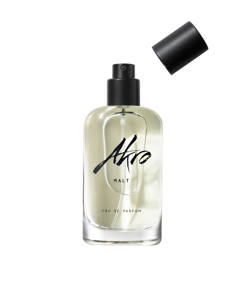 MALT by Akro, a clear glass bottle of Eau de Parfum with a black spray pump, has its cap placed slightly askew beside it, exuding a sweet and smoky scent.