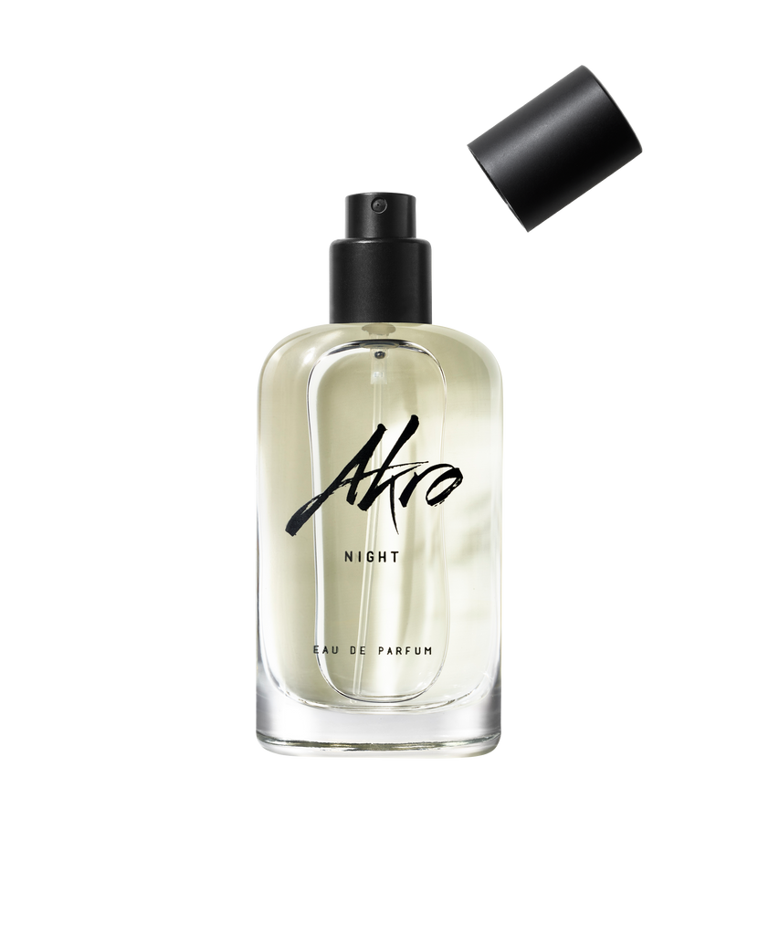 A clear glass bottle labeled "Akro NIGHT Eau de Parfum" with a black spray nozzle and a detached black cap, featuring musky notes and the essence of Bulgarian rose.