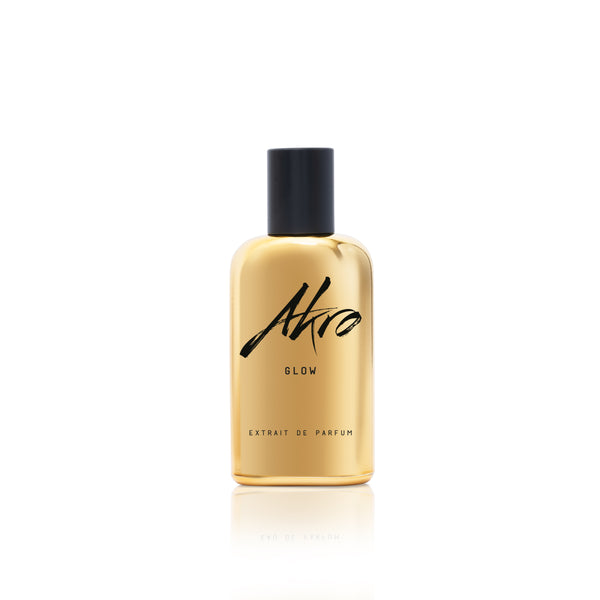 A bottle of Akro GLOW Extrait de Parfum, gold with a black cap, displayed against a white background.