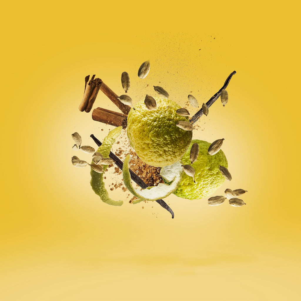 A floating composition of citrus peels, cardamom pods, cinnamon sticks, and a vanilla bean against a yellow background evokes the citrusy top notes of Xerjoff's Erba Gold creation.