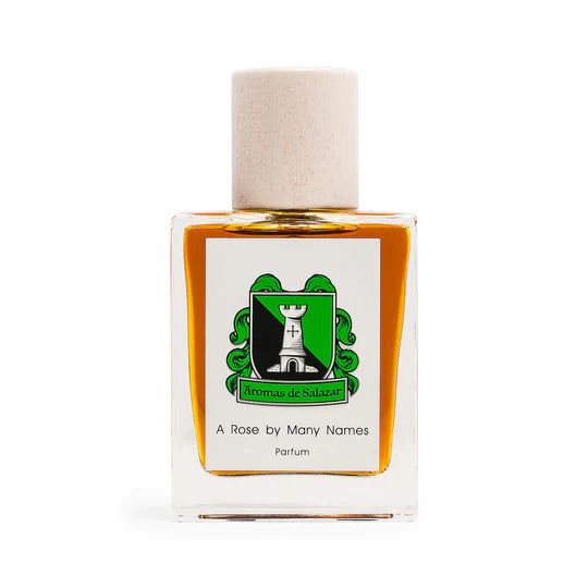 A square glass bottle of rose perfume labeled "A Rose by Many Names" by Aromas de Salazar, featuring a white cap and a green and black crest on the front.