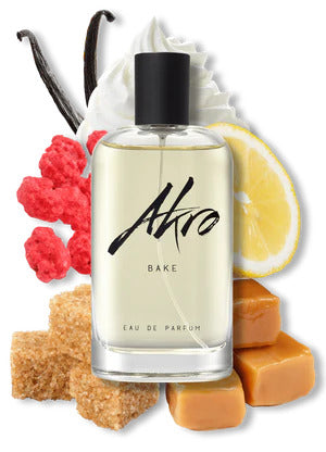 A bottle of Akro BAKE eau de parfum is surrounded by vanilla beans, a swirl of whipped cream, a lemon slice, red sugar candy, brown sugar cubes, and caramel pieces, conjuring the delectable essence of a lemon cupcake gourmand fragrance.