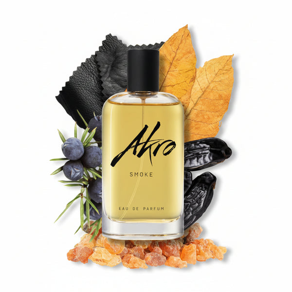 A bottle of Akro SMOKE Eau de Parfum, an aromatic unisex fragrance, is surrounded by various ingredients including leaves, spices, and dark beans.
