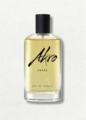 A bottle of Akro AWAKE Eau de Parfum with a black cap and clear glass container filled with light yellow liquid. The label features black cursive text, capturing the essence of a coffee fragrance in this unisex perfume.