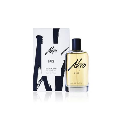 A bottle of BAKE by Akro, a delightful cupcake fragrance, stands in front of its white packaging box adorned with black abstract artwork and text.