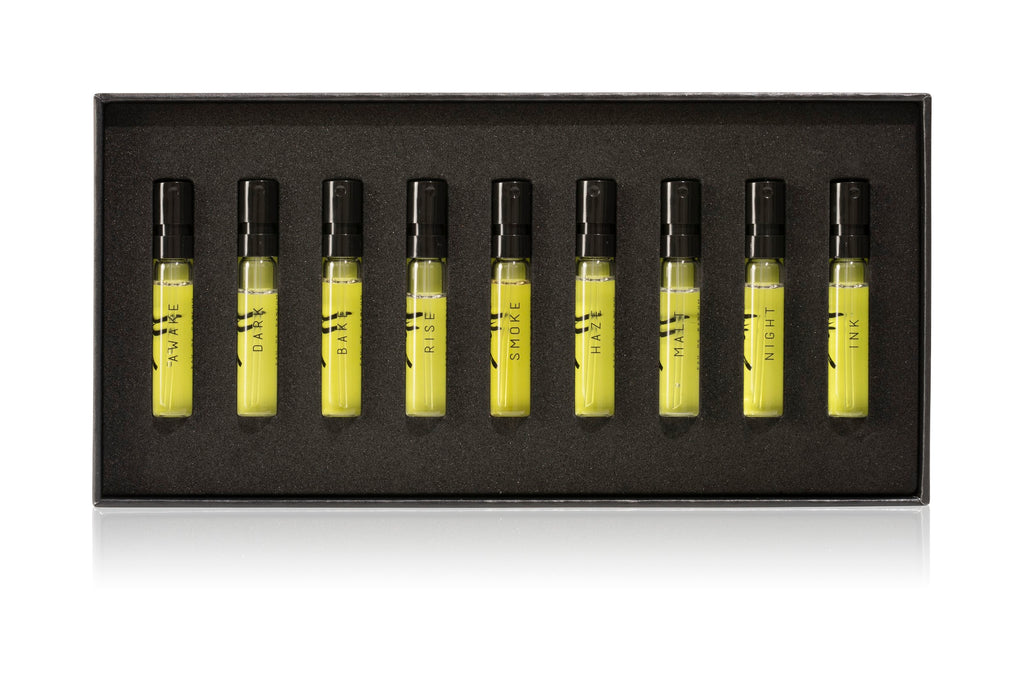 The AKRO 9 x 2ml Discovery Kit by Akro features nine perfume sample vials, labeled: HAZE, DARK, BAR, RISE, SMOKE, HALF, MALT, NIGHT, and INK. These indulgent scents are arranged neatly in a black rectangular box.